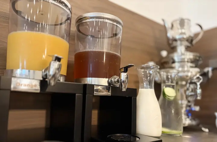 Saftspender mit Orangen- und Apfelsaft, Milchkaraffe und Samowar an der Getränkestation