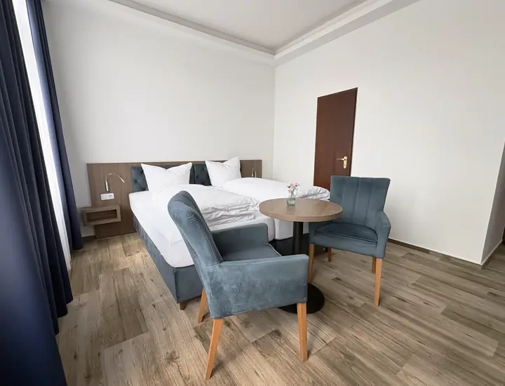 Doppelzimmer in Blau: Bett, Sitzecke mit kleinem Tisch und zwei Fenster