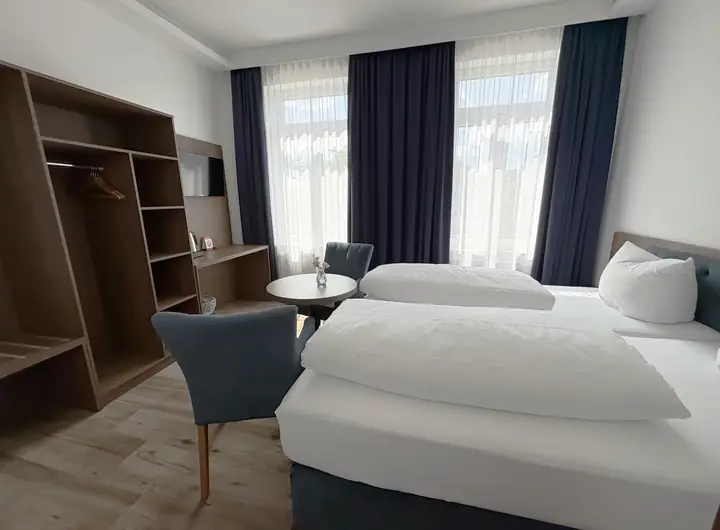 Doppelbett mit weißer Bettwäsche vor blauen Vorhängen