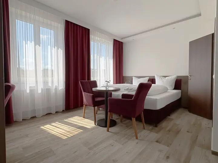 Familienzimmer in Weinrot: Bett, Sitzecke und zwei Fenster
